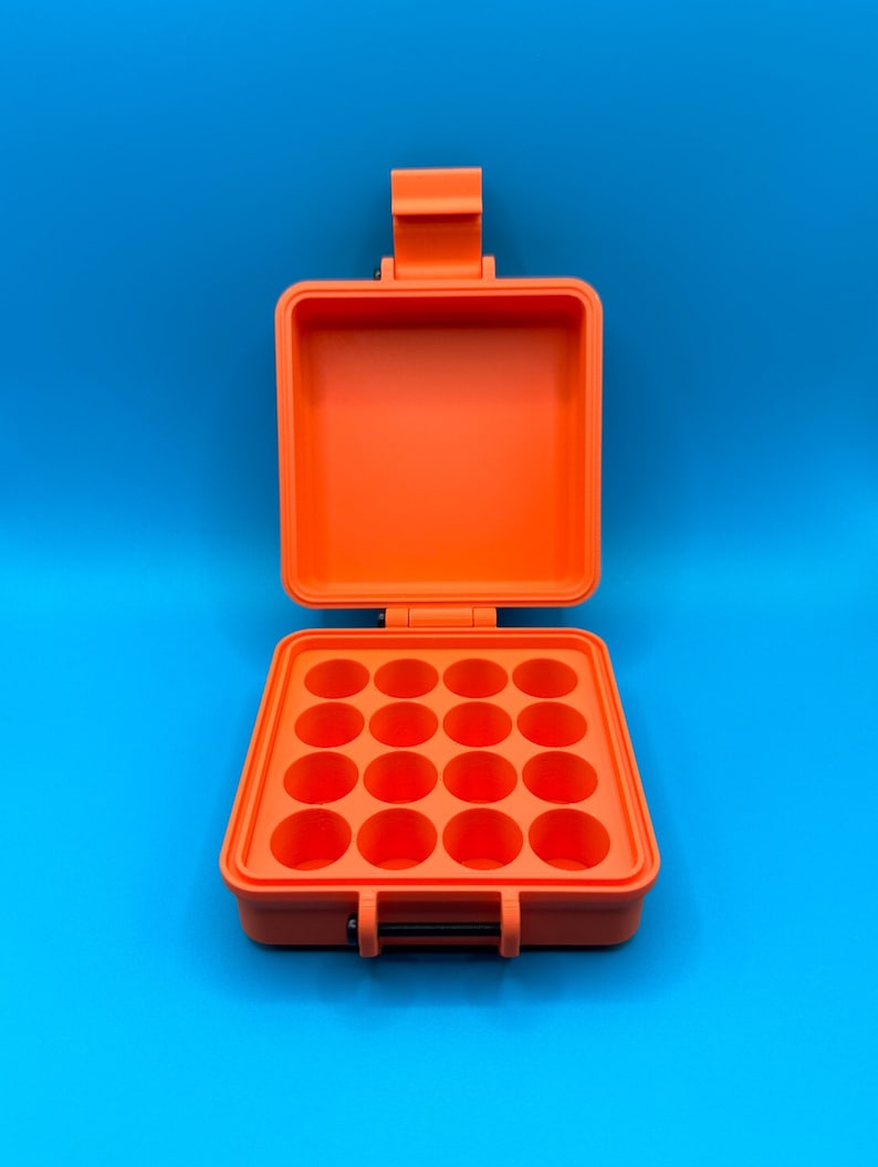 May include: A bright orange, square, hard-shell storage case with a hinged lid. The interior base features a grid of sixteen circular, recessed compartments arranged in four rows of four, designed for holding small, round items securely.