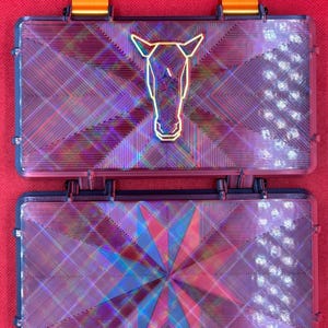 May include: Two iridescent purple and blue plastic boxes with a geometric pattern. The top box has a gold horse head design.