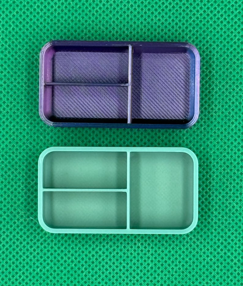 May include: Two rectangular, divided containers. The top container is a gradient of purple and blue, with a textured interior. The bottom container is a solid light green color. Both have rounded corners and are divided into three compartments.