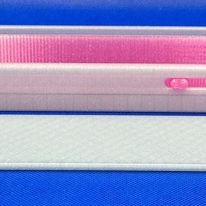 May include: A rectangular, translucent white plastic storage box with a vibrant pink interior lining. The box features a sliding mechanism on the side and comes with a separate, matching translucent white lid that has a textured, cross-hatched surface pattern.