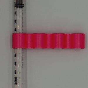 May include: A clear syringe with orange caps and a hot pink holder. The syringe has black markings indicating measurements. The pink holder has a series of rounded ridges.