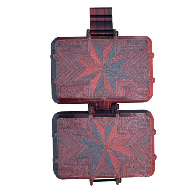 Puede incluir: Un estuche de almacenamiento rectangular de dos compartimentos con dise&ntilde;o de bisagra. Las superficies exteriores presentan un degradado de negro intenso y rojo vibrante, con un patr&oacute;n de estrella geom&eacute;trico grabado en el pl&aacute;stico.