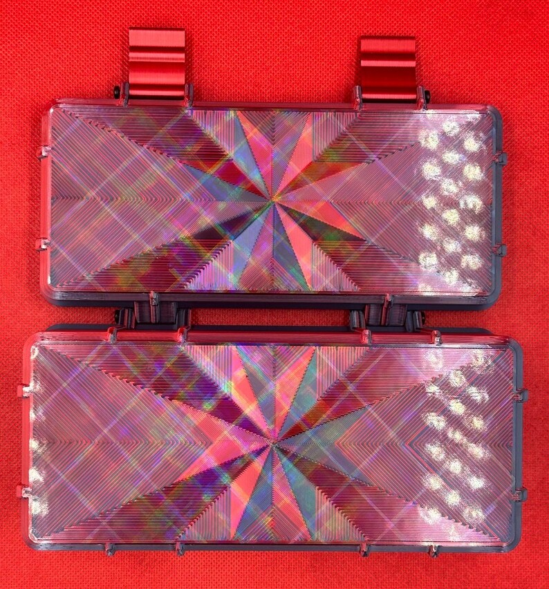 Puede incluir: Dos cajas de almacenamiento rectangulares de color oscuro con tapas abatibles, cada una con una superficie superior hologr&aacute;fica con patr&oacute;n de estrella que refleja la luz en varios colores. Tienen clips met&aacute;licos rojos en los bordes.