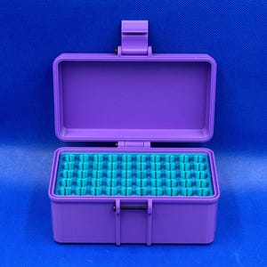 May include: A rectangular purple storage case with a hinged lid and a secure latch mechanism. The interior features a bright teal insert with a grid of numerous small, circular, vertical compartments designed for organized storage.