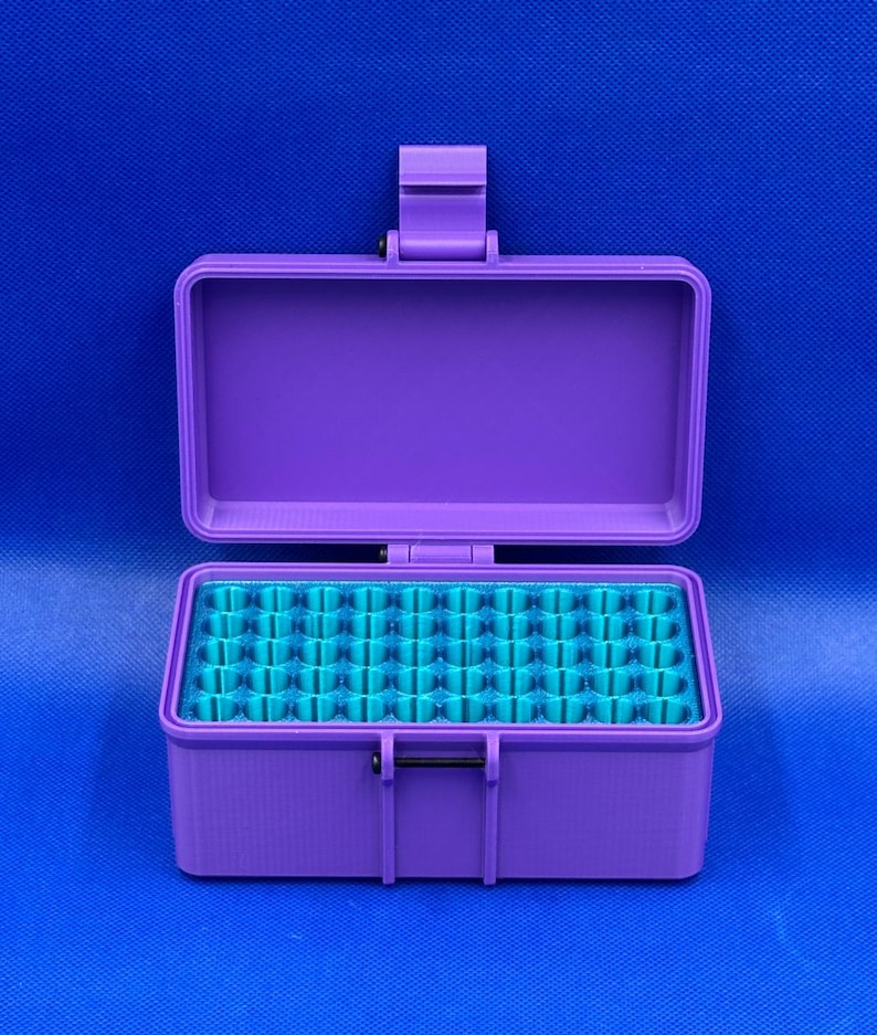 May include: A rectangular purple storage case with a hinged lid and a secure latch mechanism. The interior features a bright teal insert with a grid of numerous small, circular, vertical compartments designed for organized storage.