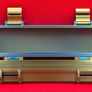 May include: A gold-colored metal box with a latch and a textured surface. The box is open and the inside is empty.