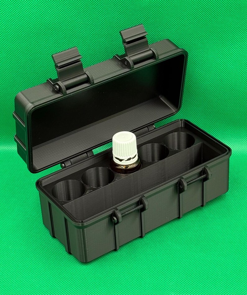 Puede incluir: Un estuche de almacenamiento rectangular negro con tapa abatible y dos cierres de pestillo. El interior cuenta con un inserto moldeado con cinco compartimentos circulares, uno de los cuales contiene un frasco de vidrio marr&oacute;n.