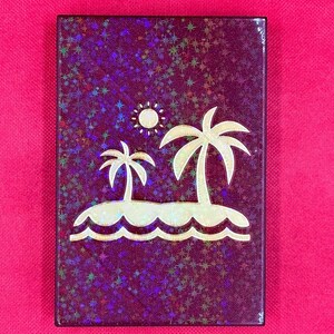 K&ouml;nnte beinhalten: Eine violette Karte mit einem goldenen Glitzerhintergrund und einem Design aus zwei Palmen auf einer Insel mit einer Sonne dar&uuml;ber.