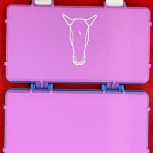 May include: Two stacked, rectangular, purple plastic boxes with white latches. The top box has a white geometric horse design on the front.