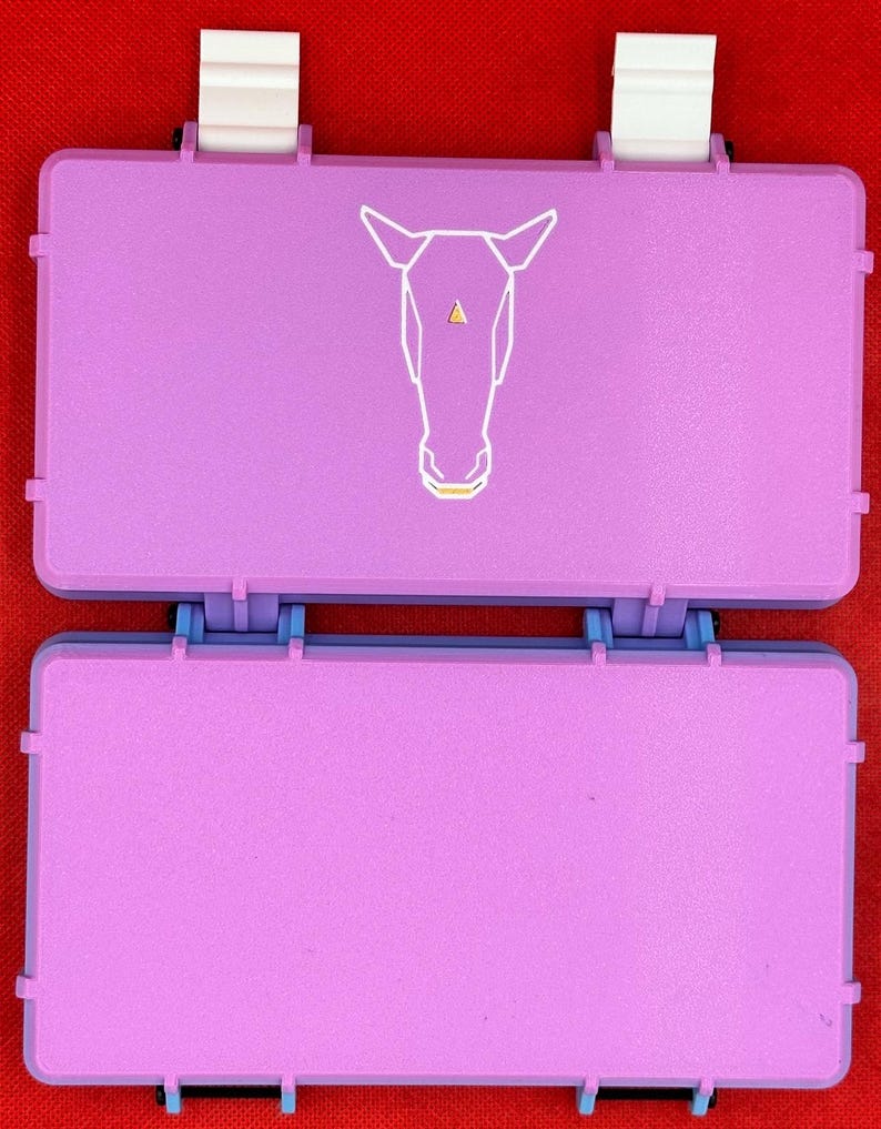 May include: Two stacked, rectangular, purple plastic boxes with white latches. The top box has a white geometric horse design on the front.