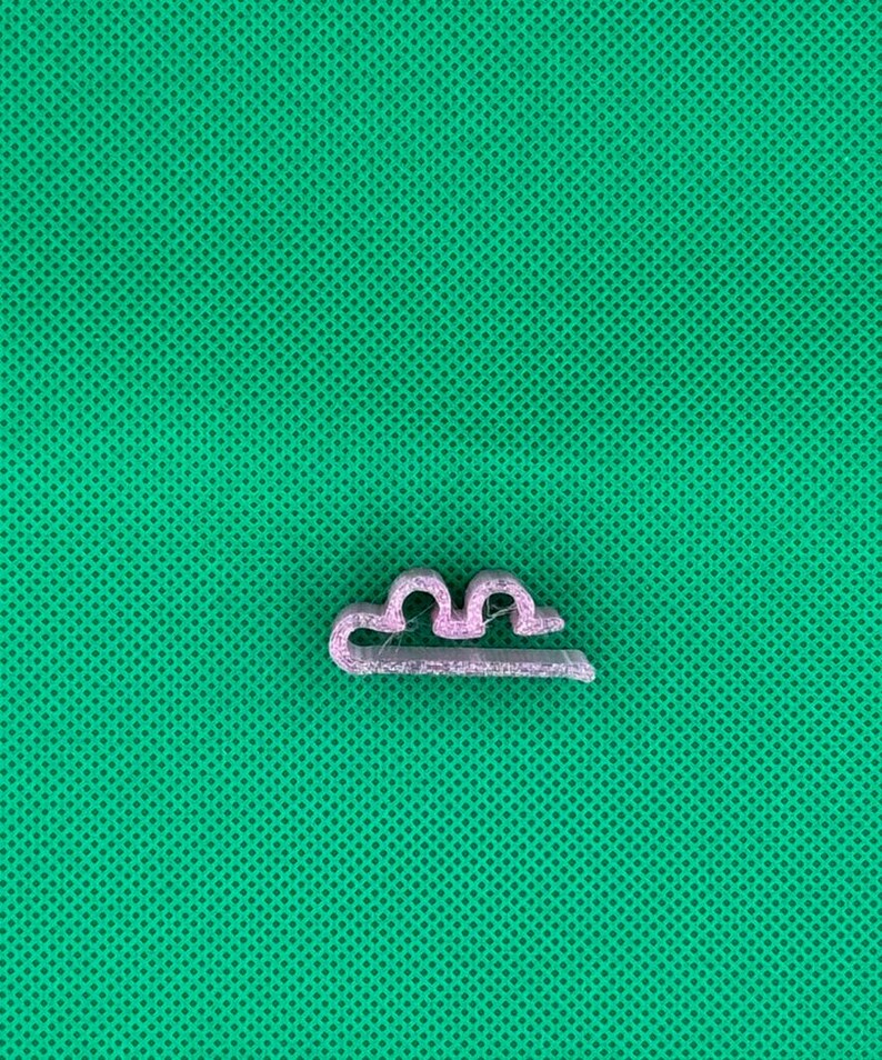 May include: A small, light pink plastic clip with a wavy design. The clip is designed to hold items together.