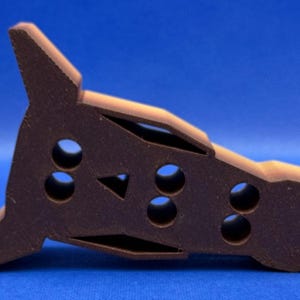 May include: A brown plastic toy shaped like a rocket with a pointed nose and a rounded tail. The toy has several holes in the side, and a triangular cutout on the top.