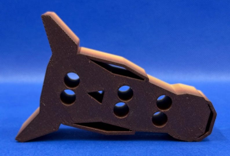 May include: A brown plastic toy shaped like a rocket with a pointed nose and a rounded tail. The toy has several holes in the side, and a triangular cutout on the top.