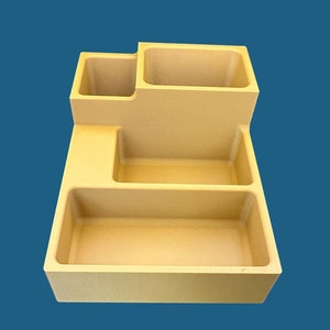 Op de afbeelding: Een beige plastic organizer met vier vakken. De organizer heeft een rechthoekige vorm met een verhoogd gedeelte aan de achterkant.