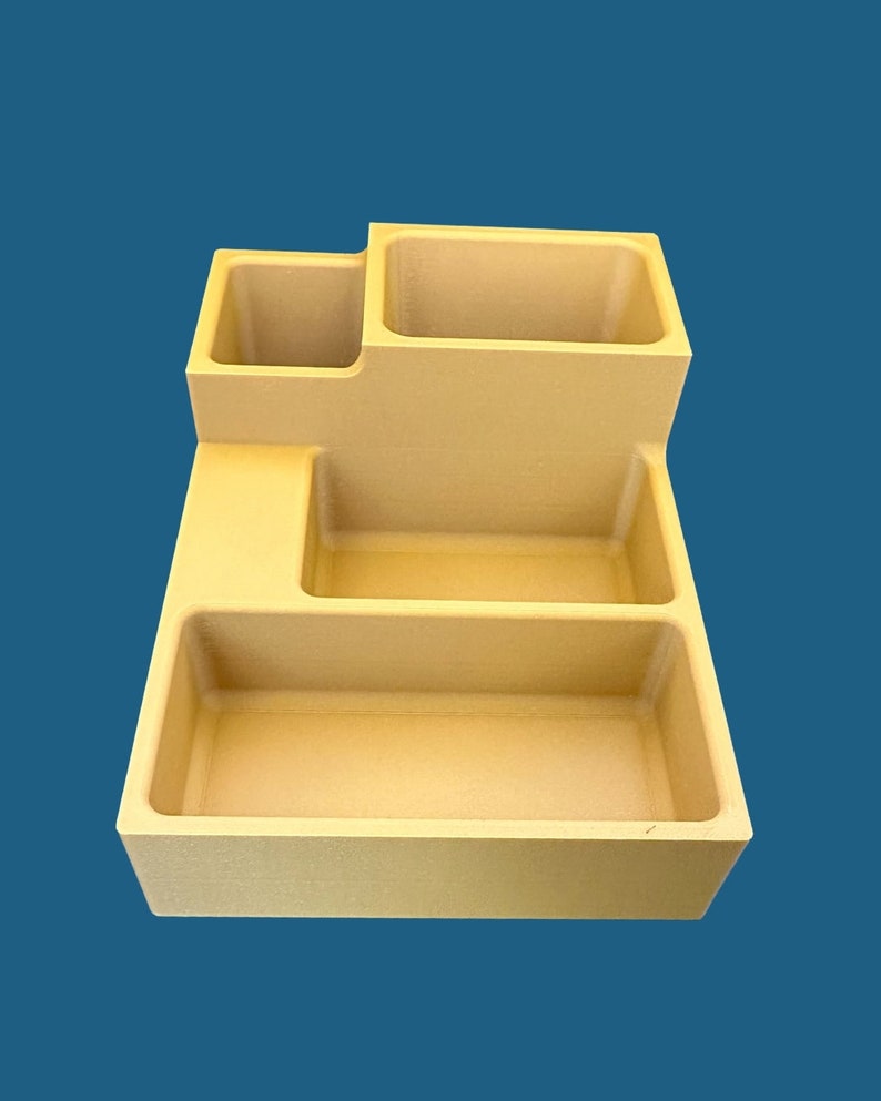 Op de afbeelding: Een beige plastic organizer met vier vakken. De organizer heeft een rechthoekige vorm met een verhoogd gedeelte aan de achterkant.
