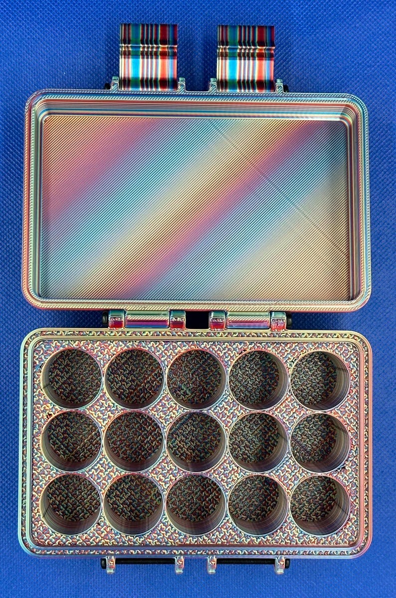 May include: A rectangular storage case with a hinged lid, featuring a multi-colored iridescent finish. The interior base contains fifteen circular compartments arranged in three rows of five, while the lid interior is smooth and flat.