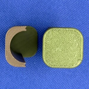 May include: Two 3D printed objects, one is a brown half-cylinder and the other is a square with a green textured surface.