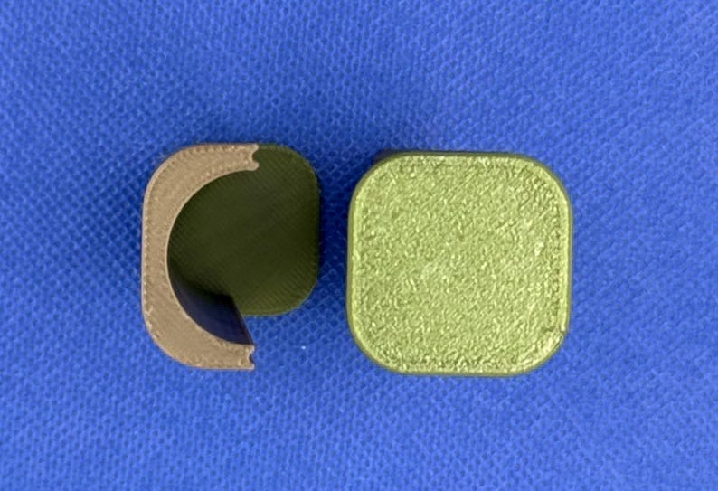 May include: Two 3D printed objects, one is a brown half-cylinder and the other is a square with a green textured surface.