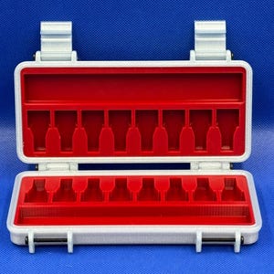 May include: A rectangular silver-colored storage case with a hinged lid and two latches. The interior features a bright red insert with ten vertical slots designed for holding small items, plus a long horizontal compartment at the base.