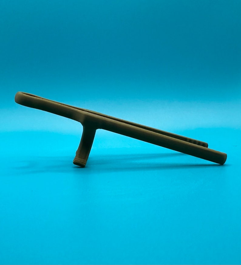 May include: A matte brown, elongated, slender object with a central support strut, resembling a stylized stand or holder. The item features a smooth, uniform surface texture and a horizontal orientation, resting on its single vertical base.