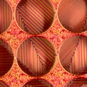 May include: A close-up of a woven basket with multiple circular openings. The basket is made of thin, red and yellow strips of material, creating a striped pattern.