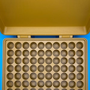 May include: A gold-colored storage case featuring an open lid and a base with a grid of sixty circular indentations. The interior is structured with a uniform pattern of holes designed for holding small items, all contained within a rectangular frame.