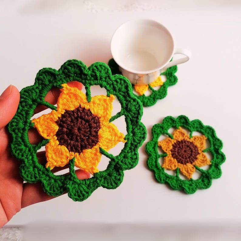 May include: Three crocheted sunflower coasters in green, yellow, and brown. The coasters are round and have a scalloped edge.