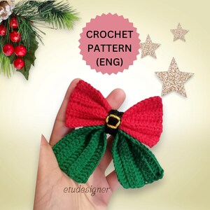 May include: Crochet pattern for a red and green bow with a black belt. The pattern is in English. The image includes the text "CROCHET PATTERN (ENG)".