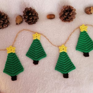 Puede incluir: Una guirnalda de árboles de Navidad de crochet verde con estrellas amarillas sobre un fondo blanco peludo.