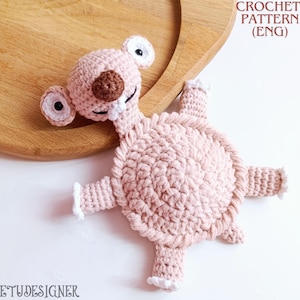 Könnte beinhalten: Ein handgefertigtes Häkeltier in Form eines hellrosa Aliens mit weißen und braunen Akzenten. Das Spielzeug hat große Augen, einen kleinen Mund und vier Gliedmaßen. Der Text "CROCHET PATTERN (ENG)" ist sichtbar.