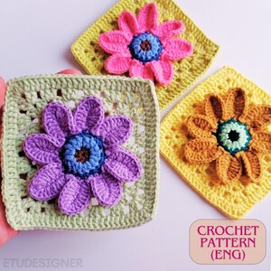 May include: Three crocheted flower squares in shades of pink, purple, and orange, each with a contrasting blue center. The squares are set on a white surface, with a light green and yellow background. The text "CROCHET PATTERN (ENG)" is visible.