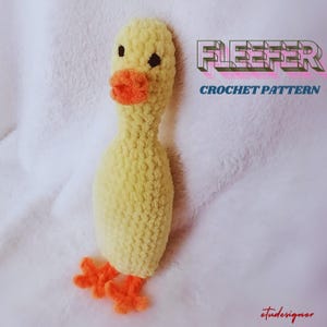 May include: A crocheted yellow duck with orange feet. The duck is lying on a white fluffy surface. The text "FLEEFER CROCHET PATTERN" is in the upper right corner of the image.