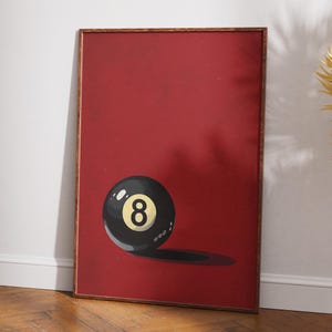 May include: A framed print of a black and white eight ball on a red background. The eight ball has a yellow number eight on it.