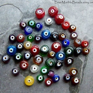 May include: A collection of colorful glass beads with an eye-like design. The beads are in various colors, including red, blue, green, and yellow, with a white center. The Etsy shop name "BlueMarbleBeads.etsy.com" is visible in the top right corner.