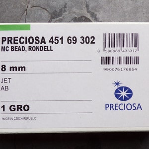 Puede incluir: Una caja blanca con el texto "PRECIOSA 451 69 302 MC BEAD, RONDELL" y "8 mm". La caja tambi&eacute;n incluye el texto "JET AB" y "1 GRO". El logotipo de Preciosa es visible. Fabricado en la Rep&uacute;blica Checa.