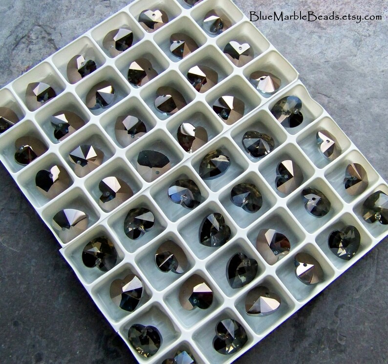 May include: A white plastic storage box filled with clear crystal heart-shaped beads. The beads are arranged in rows and columns, and they are all the same size. The box is labeled "BlueMarbleBeads.etsy.com".
