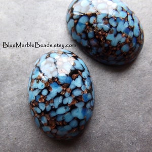 May include: Two oval-shaped glass cabochons with a blue, black, and copper speckled pattern. The cabochons are approximately 25mm in length.