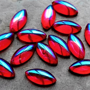 Puede incluir: Un grupo de 14 cabujones ovalados de vidrio rojo iridiscente. Los cabujones tienen un brillo iridiscente azul.