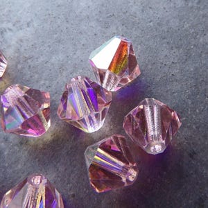 May include: A group of iridescent pink faceted glass beads. The beads have a rainbow sheen and are shaped like a pyramid.