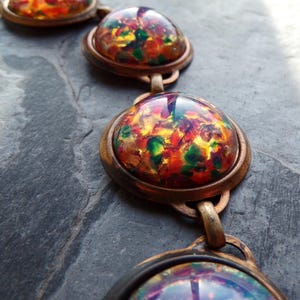 May include: A necklace with four round, iridescent, multi-colored glass cabochons set in antique brass bezels. The cabochons have a speckled, marbled appearance with shades of red, orange, yellow, green, and blue.
