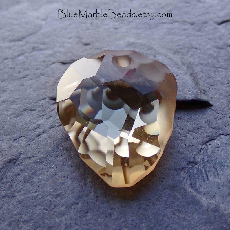 May include: A clear, faceted, teardrop-shaped pendant with a brown and white marbled pattern. The pendant has a hole at the top for stringing.