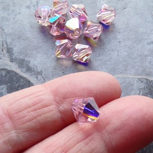 May include: A group of pink iridescent glass beads with a faceted design. The beads are approximately 4mm in size.