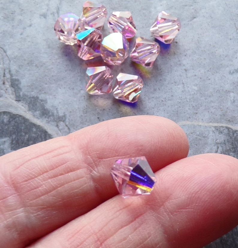 May include: A group of pink iridescent glass beads with a faceted design. The beads are approximately 4mm in size.