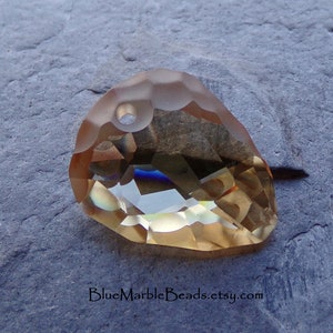May include: A faceted, teardrop-shaped crystal pendant in a light amber color with a hole at the top for stringing.