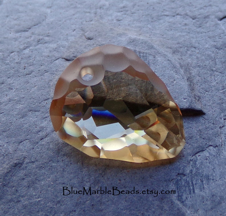 May include: A faceted, teardrop-shaped crystal pendant in a light amber color with a hole at the top for stringing.