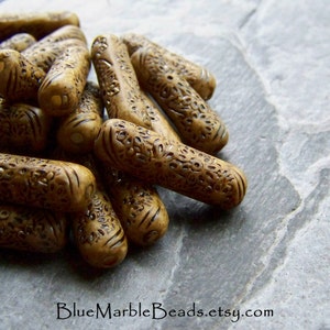 May include: A close-up of a pile of brown wooden beads with intricate carved designs. The beads are cylindrical and have a smooth, polished finish.