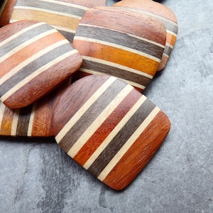 May include: A pile of wooden buttons with a striped pattern in shades of brown, orange, and white. The buttons are arranged in a random pattern on a gray surface.