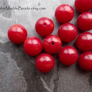 May include: A group of 12 red round beads with a shimmery finish. The beads are approximately 2 cm in diameter.