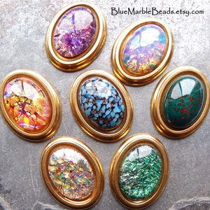May include: Seven oval-shaped glass cabochons with different patterns and colors, set in gold-toned metal frames. The cabochons feature iridescent, speckled, and marbled designs in shades of blue, green, purple, and orange.