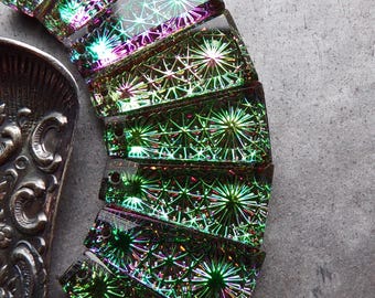 May include: A collection of seven rectangular glass pendants arranged in a fan shape, each featuring a holographic starburst pattern in shades of green, purple, and gold. The text BlueMarbleBeads.etsy.com is visible at the top of the image.